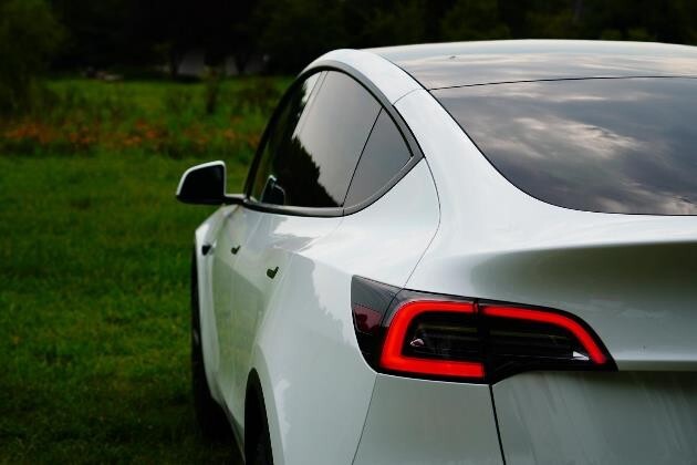 A white Tesla Model Y parked on grass outdoors, representing Tesla-approved repair services.