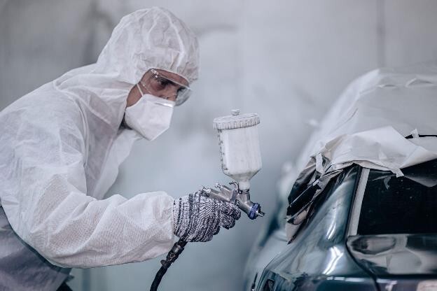 A worker in full gear re-spraying a Tesla which is part of Tesla approved body repair services.