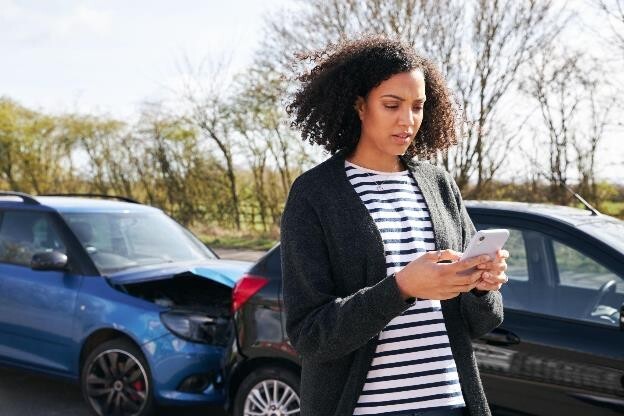 A woman who has just had a car accident using her phone and following all of the steps to take after a car accident.