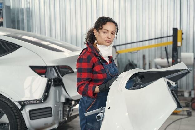 A mechanic carrying out Tesla collision repair procedures on a white Tesla in a garage.