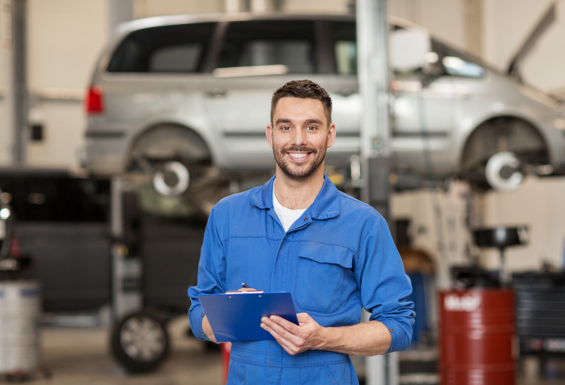 A smiling mechanic in a repair shop that offers car accident management. 