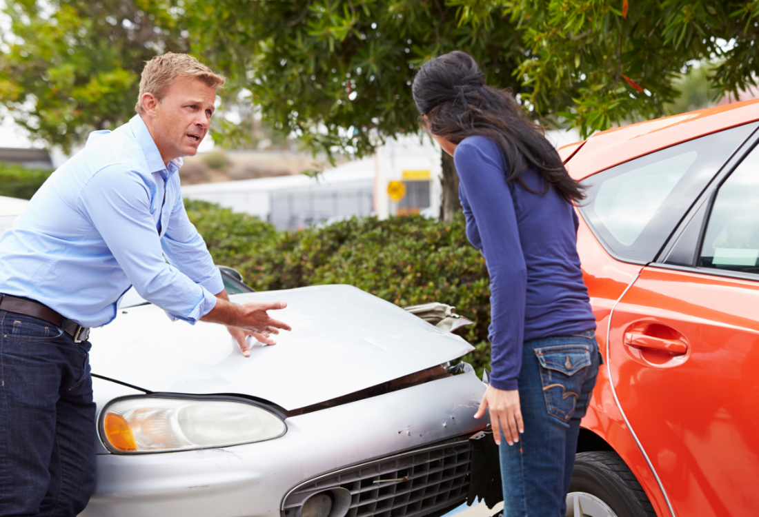 Two drivers standing beside their damaged cars after a collision, discussing the accident and inspecting the vehicles.