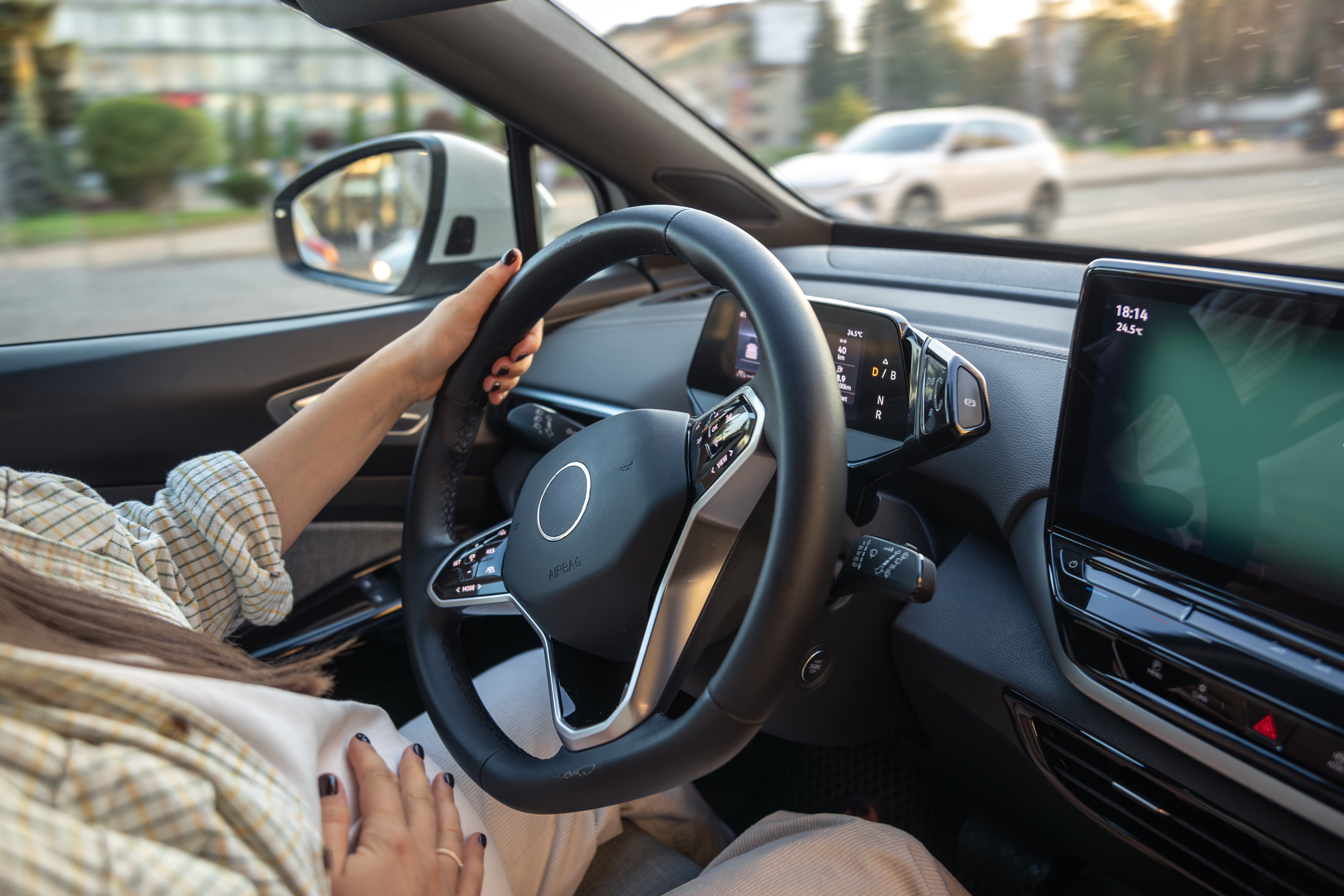 Driver's hand on the steering wheel of a car with a digital dashboard display.